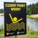 Tablica „Czarny Punkt Wodny" oznaczająca niebezpieczne miejsce kąpieli nad jeziorem